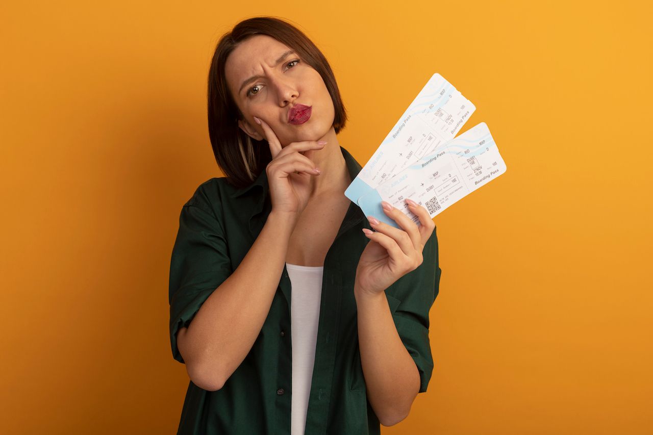 confused-pretty-caucasian-woman-puts-finger-face-holds-air-tickets-orange.jpg