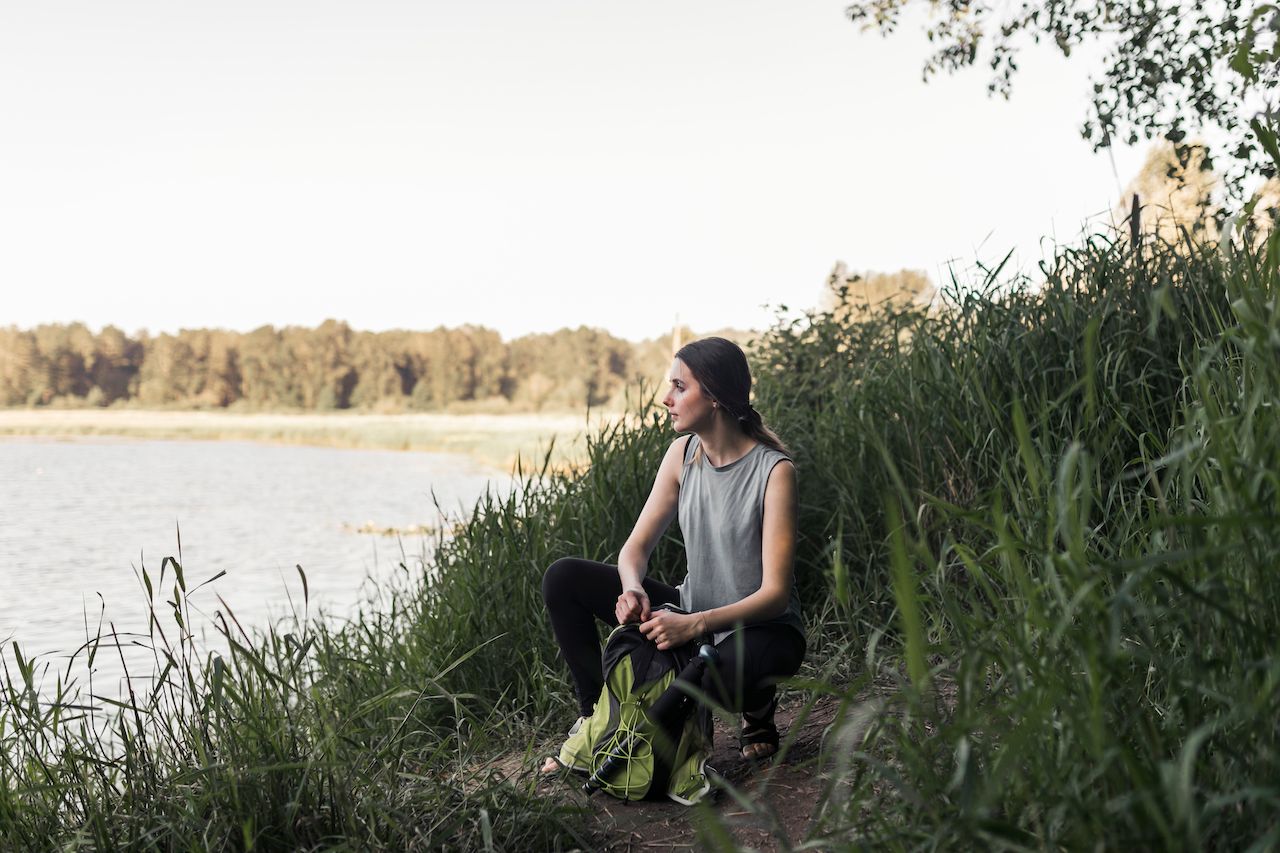 fitness-young-woman-with-her-backpack-crouching-near-lake.jpg